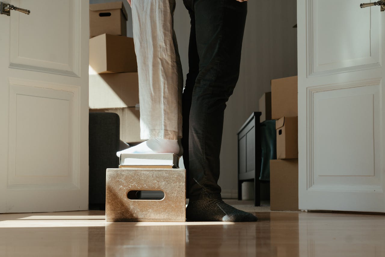 A couple standing on a box surrounded by moving cartons, symbolizing home relocation.